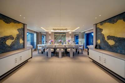 A long, elegant dining table set for a meal is centered in a luxurious room with abstract art on the walls and white cabinets lining the foreground.