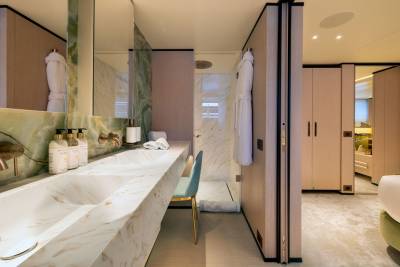 A luxurious bathroom with a marble vanity and sink in the foreground, and a bedroom with soft lighting and elegant furnishings in the background.