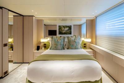 A neatly made bed with floral pillows is in the foreground, while mirrored closets and a large window with blinds fill the background of this luxurious cabin.