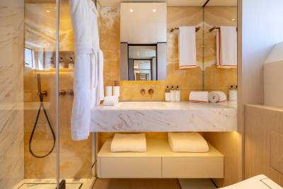 A luxurious bathroom features a marble vanity with folded towels in the foreground and a backlit onyx wall in the background.