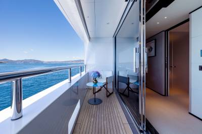 A small table with a floral arrangement sits on a yacht's deck overlooking the ocean and distant hills.