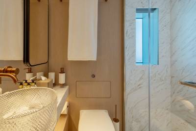 A modern bathroom features a textured glass sink in the foreground and a marble-tiled shower with a blue-lit niche in the background.