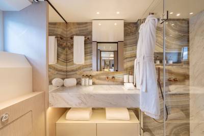 A luxurious bathroom features a marble vanity with toiletries in the foreground and a marble-tiled shower with a white robe hanging in the background.