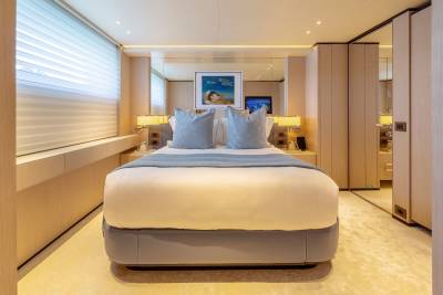 A plush bed with light blue pillows and a throw is in the foreground, while mirrored walls and wooden cabinetry form the background of this luxurious bedroom.