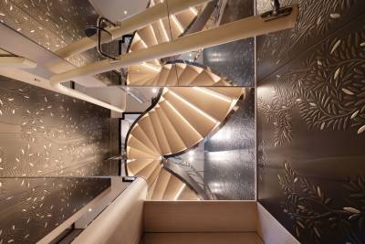 A modern spiral staircase with illuminated treads ascends through a space with intricately patterned walls.