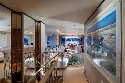 A luxurious yacht interior features a staircase in the foreground and a spacious living area with a view of the ocean in the background.