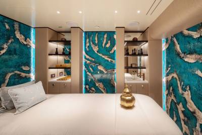 A plush bed with a golden accent piece sits in the foreground, while the background features striking turquoise and silver abstract wall art and illuminated shelves.