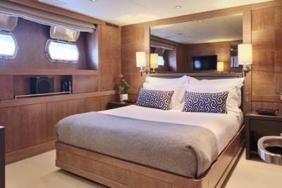A luxurious bedroom with a large bed in the foreground and a mirrored wall with a television in the background.