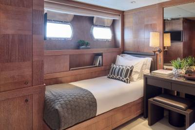 A cozy cabin with a twin bed in the foreground and a desk with a mirror in the background.