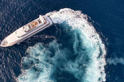 A luxurious white yacht cuts through the deep blue ocean, leaving a frothy white wake behind it.