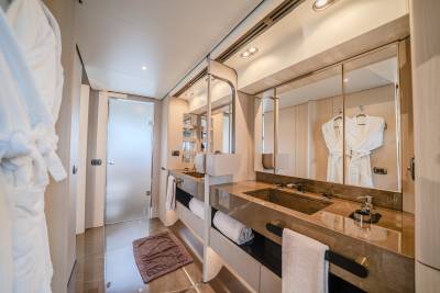 Fluffy white robes hang in the foreground of a luxurious bathroom with dual sinks and large mirrors reflecting more robes in the background.