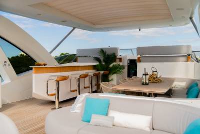 A luxurious yacht deck features a comfortable seating area in the foreground and a bar and dining table in the background, all under a covered canopy.