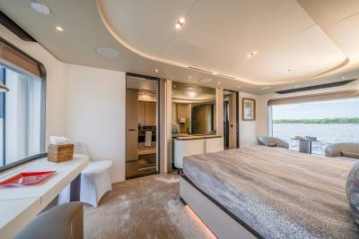 A luxurious bedroom with a large bed in the foreground and a scenic view of water through the window in the background.