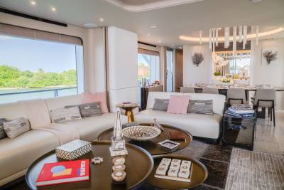 A modern yacht living room with plush white sofas and coffee tables in the foreground, and a dining area with a long table and chairs in the background.