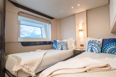 Two neatly made twin beds with decorative pillows are in the foreground, while a large window with a view of the sky is in the background.