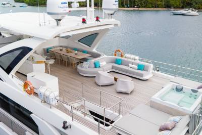 A luxurious yacht deck with a hot tub and seating area in the foreground overlooks a calm body of water with distant islands in the background.