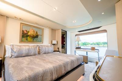 A luxurious bedroom with a large bed in the foreground and a desk by a window overlooking a calm body of water in the background.