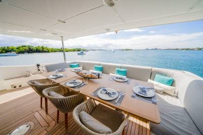 A beautifully set dining table with chairs on a yacht's deck overlooks a calm bay dotted with boats and lush green islands.