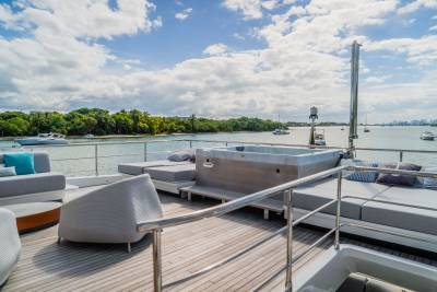 A luxurious yacht deck with a hot tub and lounge chairs in the foreground overlooks a calm bay dotted with boats and a distant city skyline.