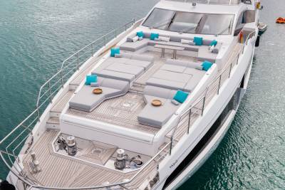 A luxurious white yacht with plush gray seating and bright turquoise cushions is docked in calm, blue water.