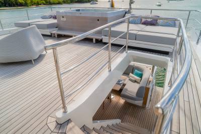 A luxurious yacht deck with a hot tub and lounge seating in the foreground, and a calm ocean with boats in the background.