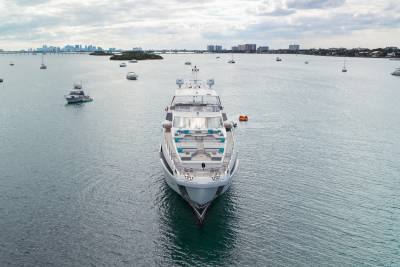 A large white yacht is anchored in calm water with a city skyline in the background.