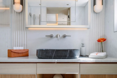 A modern bathroom vanity with a dark marble basin in the foreground is reflected in a large mirror above, with soft lighting and decorative wall panels in the background.
