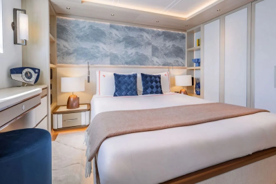 A luxurious bedroom features a neatly made bed with blue pillows and a tan throw in the foreground, while the background reveals built-in wardrobes and shelves adorned with decorative items.