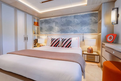A luxurious bedroom with a neatly made bed in the foreground and a modern vanity and closet in the background.