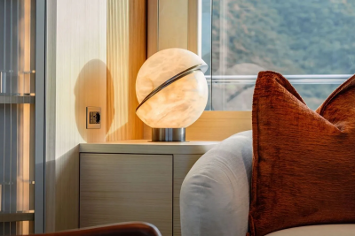 A glowing orb lamp sits on a wooden cabinet in the foreground, with a blurred green landscape visible through a window in the background.