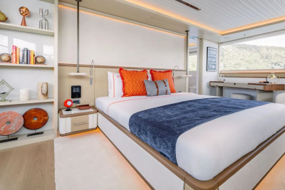 A luxurious bedroom with a large bed in the foreground and a desk and window with a view of hills in the background.