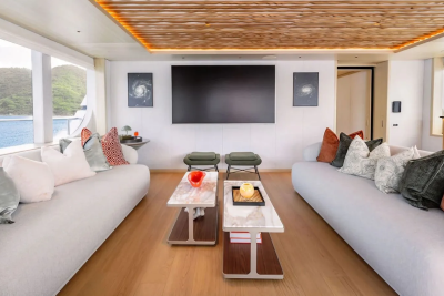 Two plush sofas flank a modern living area with a large screen TV, while large windows reveal a serene ocean view with lush green islands in the distance.