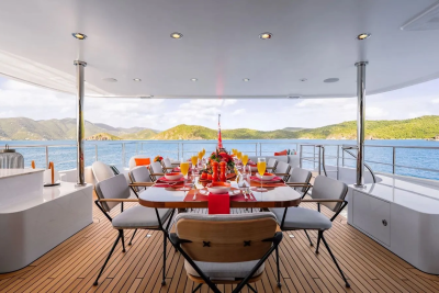 A beautifully set dining table on a yacht's deck overlooks a scenic backdrop of islands and the ocean.