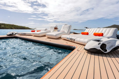 Inflatable loungers and a jet ski rest on a floating dock in the foreground, with a calm blue ocean and lush green islands in the background.