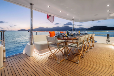 A beautifully set dining table on a yacht's deck overlooks a tranquil ocean and distant islands at sunset.