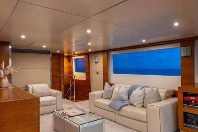 A plush living area with a sofa and armchairs in the foreground is set against a backdrop of large windows revealing a serene ocean view.