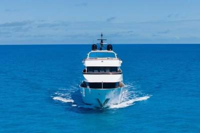 A large white yacht cruises through calm, bright blue ocean waters under a clear sky.