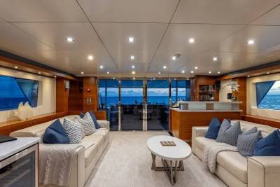 A luxurious yacht interior with plush sofas and a coffee table in the foreground, and a stunning ocean view through large windows in the background.
