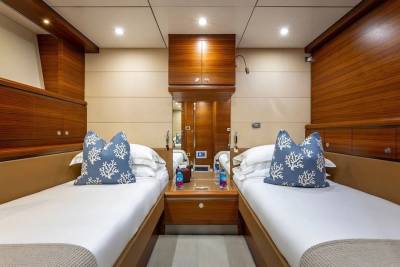 Two neatly made twin beds with blue coral-patterned pillows are in the foreground, while the background features polished wood paneling and cabinetry.