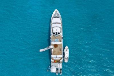 A large white yacht with a slide and a smaller boat are anchored in crystal clear turquoise water.