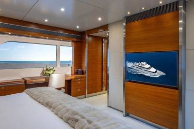 A luxurious bedroom with a large bed in the foreground and a large window overlooking the ocean in the background, with a television displaying a yacht.