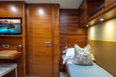 A small bed with a starfish pillow sits next to a wooden door, while a desk with a television is mounted on the wall in the foreground.