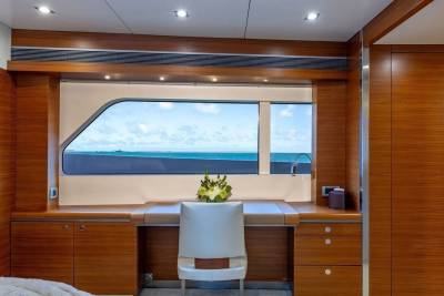 A white chair sits at a wooden desk in front of a large window overlooking a blue ocean and sky.
