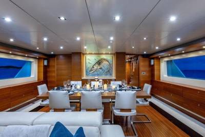 A luxurious dining room on a yacht features a set table in the foreground and a serene ocean view through large windows in the background.