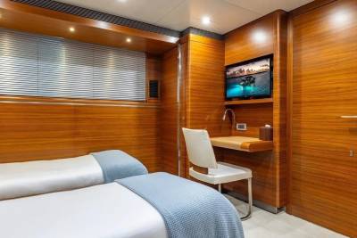 Two beds with blue blankets are in the foreground, while a television and a desk are in the background.