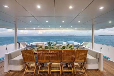 A beautifully set dining table with chairs on a yacht's deck overlooks a calm ocean under a cloudy sky.