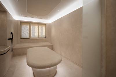 A modern spa room features a plush massage table in the foreground and a built-in bench with a window in the background.