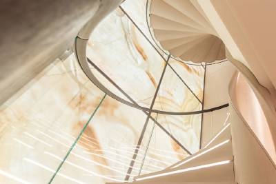 A white spiral staircase curves upwards against a backdrop of illuminated, marbled onyx.