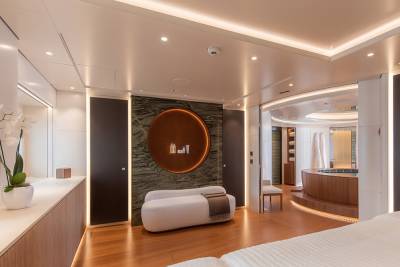A modern spa room with a white chaise lounge and orchids in the foreground, and a circular jacuzzi and treatment area in the background.