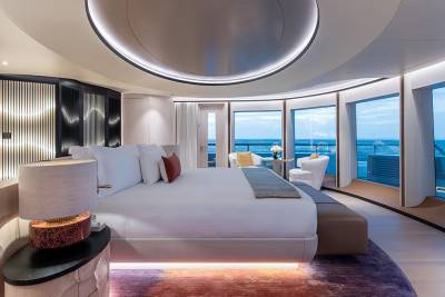 A luxurious bedroom with a large bed in the foreground and a panoramic view of the ocean through large windows in the background.